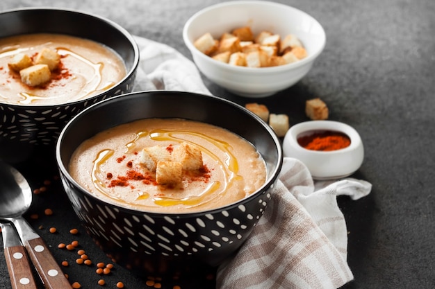 Linsencremesuppe mit Paprika und Croutons in schwarzen Keramikschalen auf dunklem Hintergrund