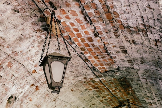 Linterna antigua de metal con cadenas cuelga de un techo de ladrillo