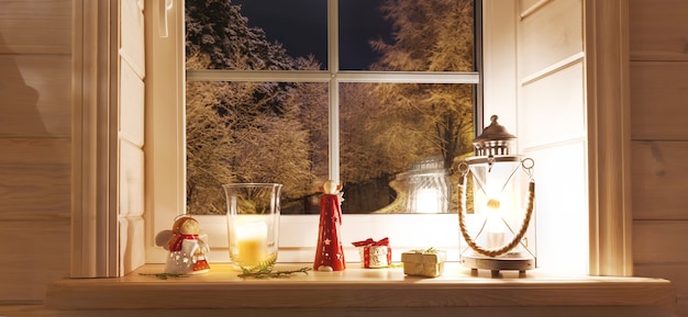 Linterna de Navidad, ángeles con regalos en la ventana de una casa de madera con vistas al jardín de invierno por la noche en invierno. Composición navideña