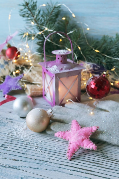 Linterna de Navidad con velas encendidas, bolas de estrellas e iluminación sobre un fondo de madera