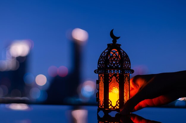 Linterna que tiene el símbolo de la luna en la parte superior sosteniendo a mano para el mes sagrado de Ramadán Kareem