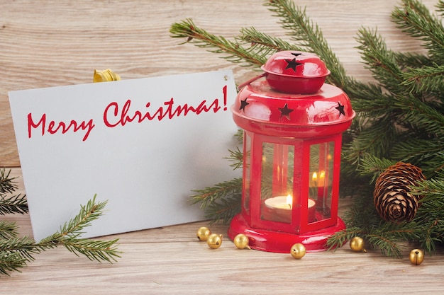 Linterna roja brillante de Navidad con tarjeta de feliz Navidad y árbol de hoja perenne y conos