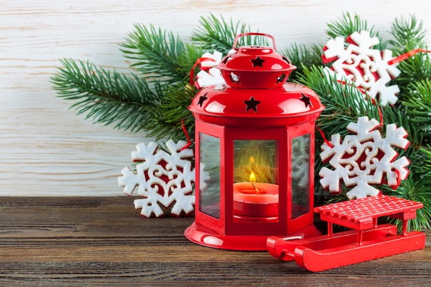 Linterna roja con una vela encendida y decoración navideña sobre fondo blanco de madera con árbol de Navidad