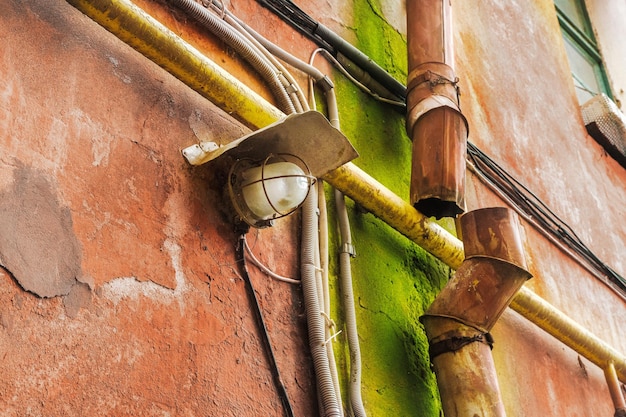 Linterna y un tubo de desagüe oxidado en la pared de una casa
