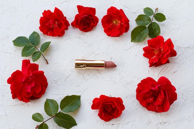 Lippenstift mit Rosenblüten und grünen Blättern auf weißem Hintergrund. Ansicht von oben.