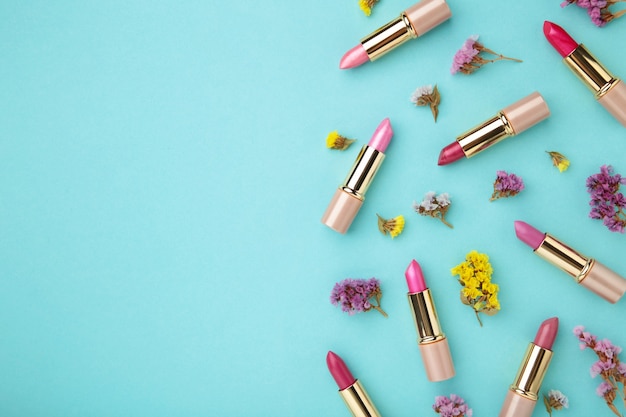 Lippenstift mit schönen Blumen auf blauem Hintergrund mit Kopienraum