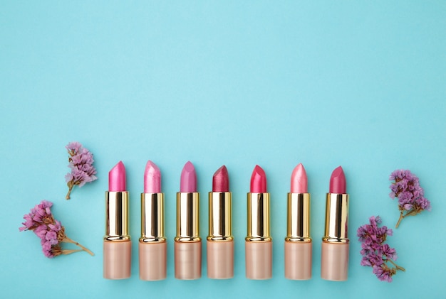 Lippenstift mit schönen Blumen auf blauem Tisch mit Kopienraum