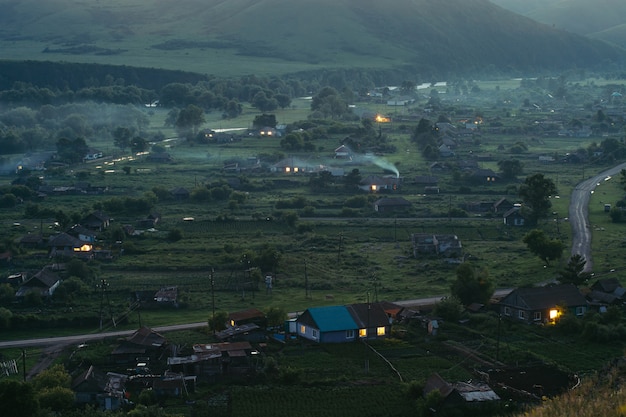 Liquidação rural nas montanhas ao entardecer. casas de madeira, cabanas aquecidas por fogões. fumaça dos canos. as colinas. altai.