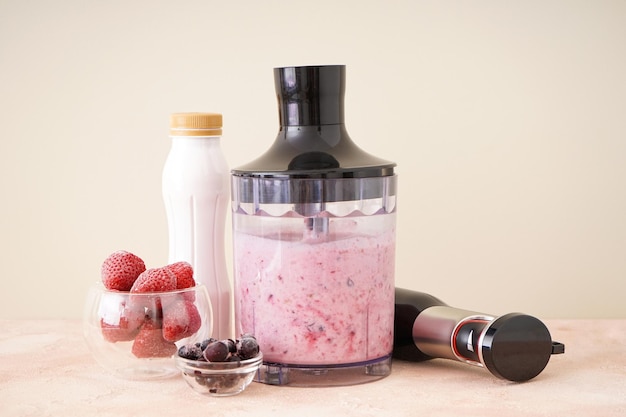 Liquidificador de mão para misturar smoothie de frutas frescas orgânicas em um fundo colorido, comida saudável.