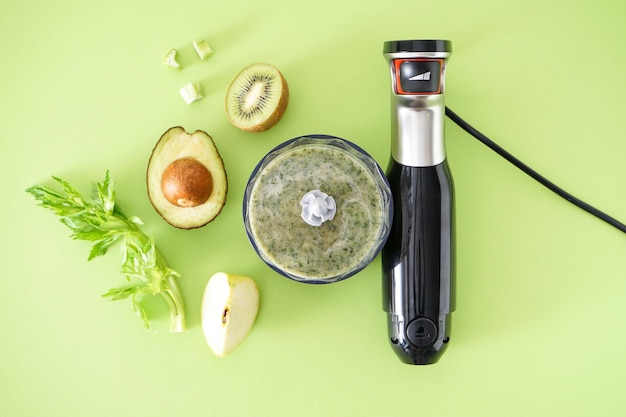 Liquidificador elétrico de plástico preto e acessórios com frutas em um fundo verde. Postura plana.