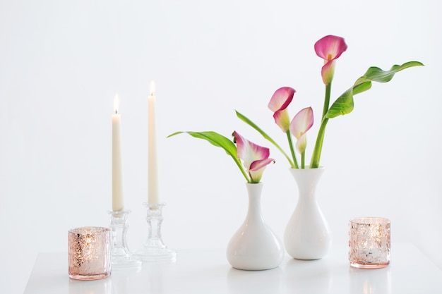 Lirio de cala rosa en florero y velas encendidas en blanco