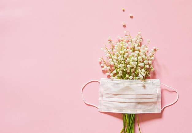 Lírios do vale e uma máscara médica em um conceito de alergia a flores de fundo rosa