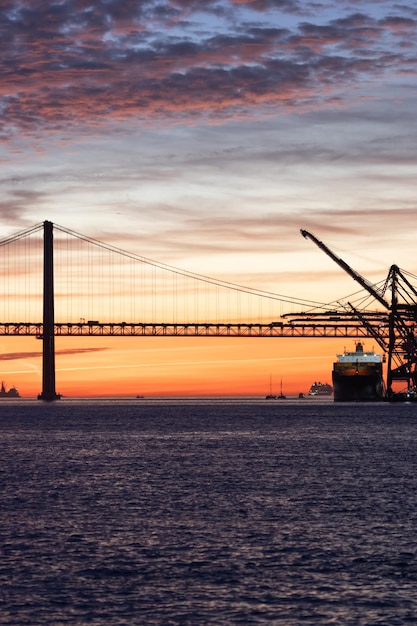 Lisboa, ponte de abril ao pôr do sol e guindastes de trabalho industrial