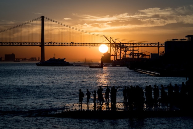 LISBOA Portugal 27 de outubro de 2017 pessoas assistindo o pôr do sol com vista na Ponte 25 de Abril no Rio Tejo perto da Praça do Comércio em Lisboa Portugal