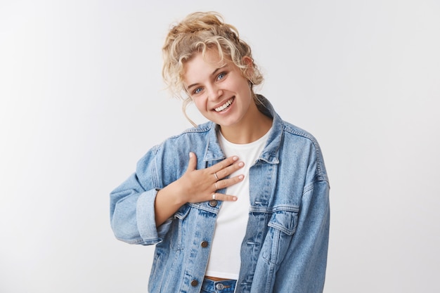 Lisonjeada fofa terna feminina jovem loira coque encaracolado olhos azuis pressione palma da mão agradecida inclinando a cabeça sorrindo satisfeito apreciando bom elogio, agradecendo ajuda, parece agradecida agradecida