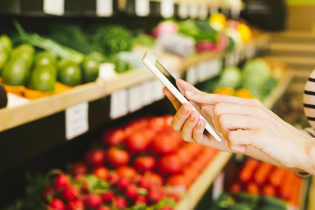 Lista de compras de frutas y verduras Mujer joven con teléfono móvil en la mano compras en tienda de alimentos saludables Teléfono en manos femeninas