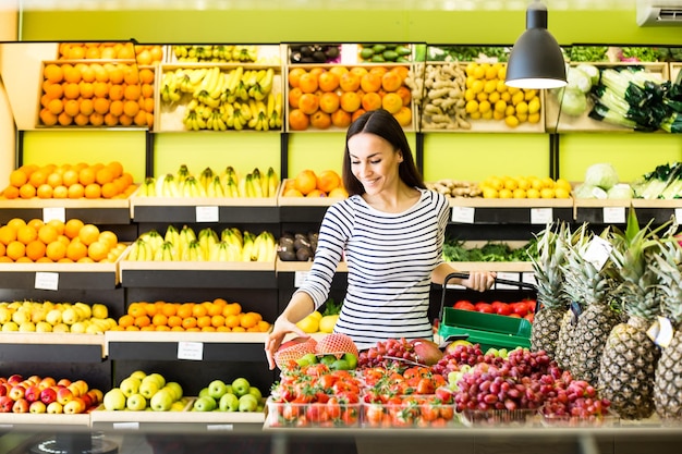 Lista de compras Hermosa mujer sonriente se para con el teléfono cerca de los productos en la tienda