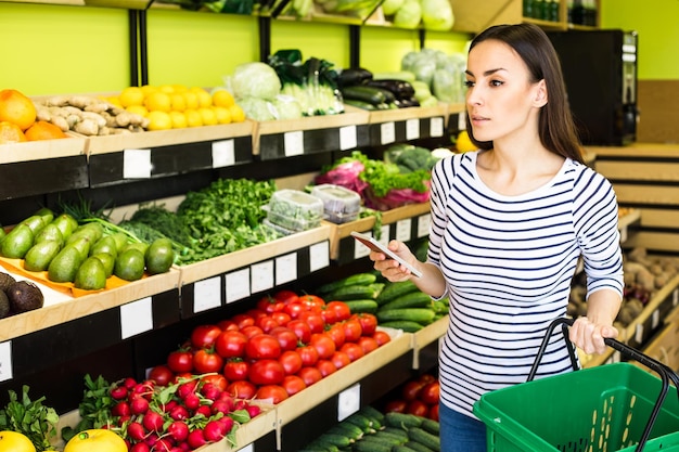 Lista de compras Mulher bonita sorridente fica com telefone perto de produtos na loja