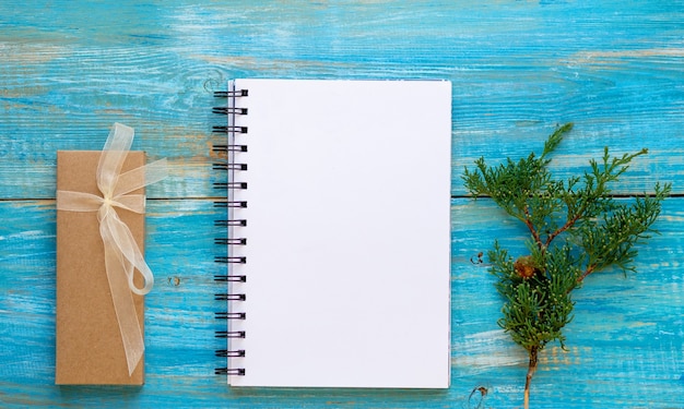 Foto lista de deseos de navidad m cuaderno de espiral a santa claus en mesa de madera azul con caja presente y rama de thuja