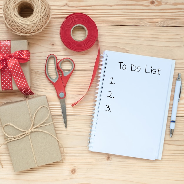 Lista de tareas con libreta, tijeras y decoración de caja de regalo en mesa de madera