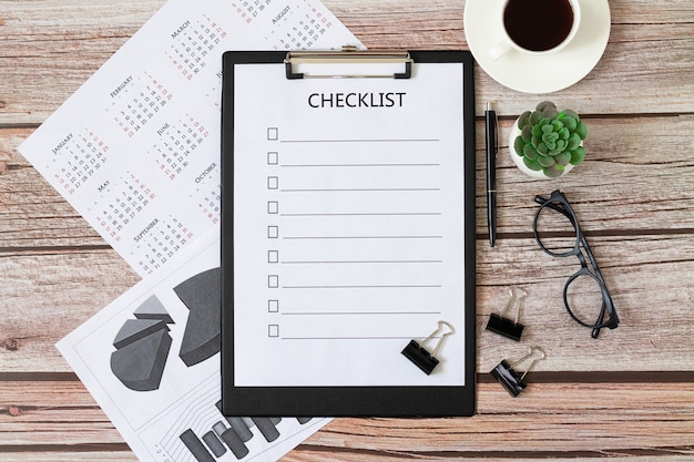 Lista de verificación en blanco en el escritorio de madera con café, vasos, calendario, plantas. Vista superior del concepto de negocio