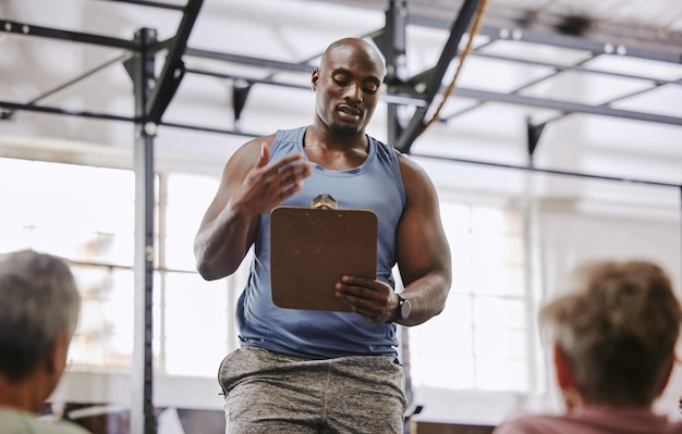 Lista de verificación del gimnasio de entrenamiento y hombre negro hablando con clientes mayores en la bienvenida de presentación de capacitación o membresía Entrenador personal entrenamiento físico o registro de programa de ejercicios y club comunitario de EE. UU.