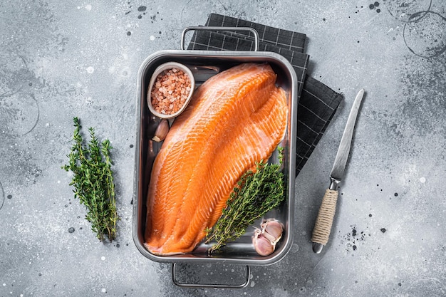 Listo para cocinar filete de salmón crudo con hierbas en bandeja de acero. Fondo gris. Vista superior.