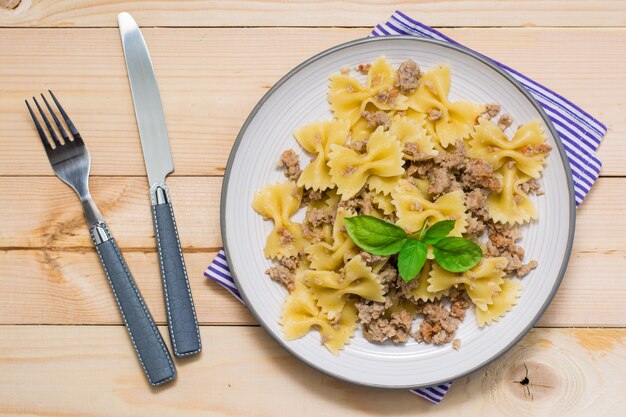 Listo para comer pasta azul marino con carne picada y hojas de albahaca en un plato y cubiertos en una mesa de madera. Cocina rusa. Vista superior