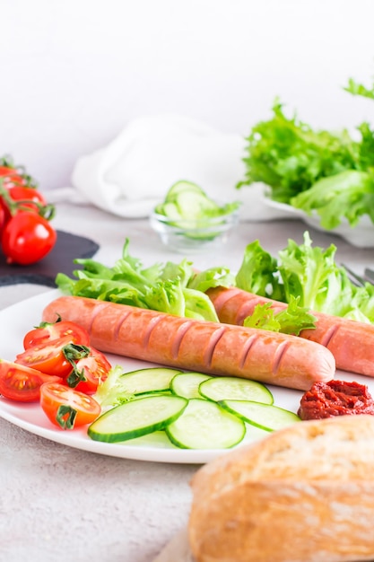 Listo para comer salchichas fritas tomates picados y verduras de pepino en un plato y un bollo en la mesa Abundante merienda casera Vista vertical