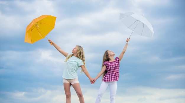 Listo para cualquier clima Chicas amigas con sombrillas Fondo de cielo nublado Pronóstico del tiempo Cambio de clima Niños despreocupados al aire libre Ventoso o lluvioso, estamos preparados Libertad y frescura