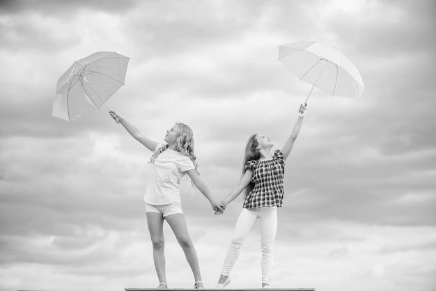 Listo para cualquier clima Ventoso o lluvioso, estamos preparados Libertad y frescura Pronóstico del clima Cambio de clima Niños despreocupados al aire libre Chicas amigas con sombrillas fondo de cielo nublado