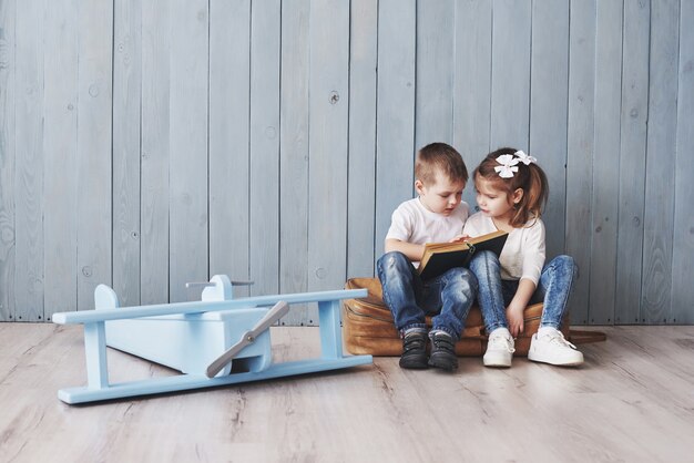 Listo para grandes viajes. Feliz niña y niño leyendo un libro interesante con un gran maletín. Concepto de libertad e imaginación