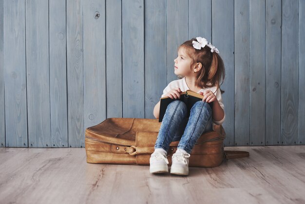 Listo para grandes viajes. Niña feliz que lee el libro interesante que lleva un maletín grande y una sonrisa. Viajes, libertad e imaginación.