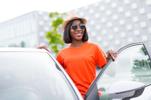 Listo para ir joven mujer negra en traje de verano y gafas de sol abriendo la puerta del coche