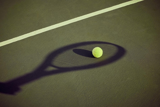 Listo para servir. Disparo de una pelota de tenis tirada en una cancha delineada por la sombra de una raqueta.