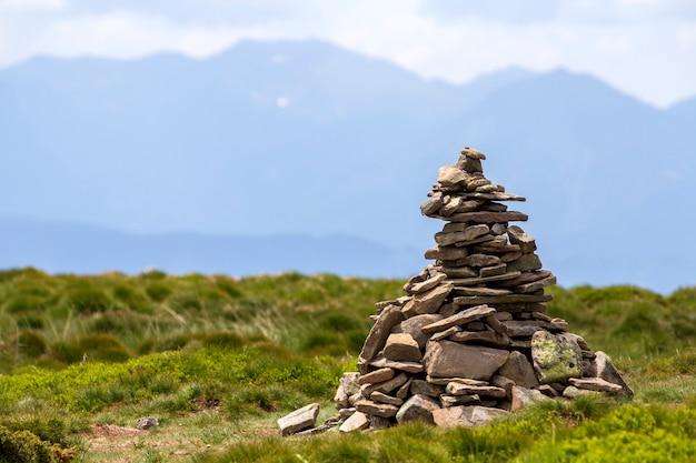 Lit pelas pedras desiguais da montanha do sol brilhante do verão empilhadas e equilibradas como a pilha da pirâmide no vale gramíneo verde na luz - céu azul branco do espaço da cópia. Turismo. Conceito de viagem e Marco.