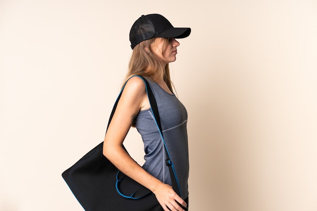 Litauische junge Sportfrau, die eine Sporttasche lokalisiert auf beigem Hintergrund hält, die unter Rückenschmerzen leidet, weil sie sich bemüht haben