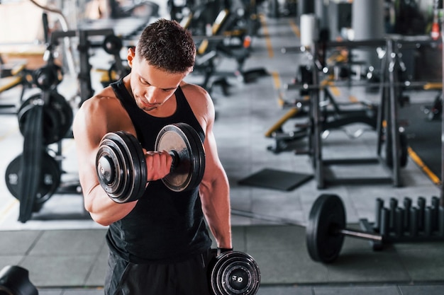 Liting mancuernas Joven deportista fuerte vestido de negro tiene un día de entrenamiento en el gimnasio