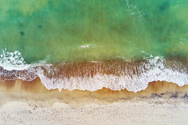 Litoral com ondas do mar azul e vista superior da praia de areia