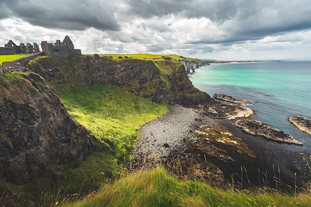 Litoral da Irlanda do Norte com o castelo dunluce à distância, uma pitoresca planície coberta de grama e