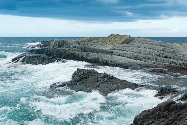 Litoral rochoso formado por basalto colunar contra o pano de fundo de uma paisagem costeira de mar tempestuoso das Ilhas Curilas