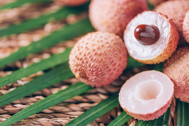 Litschi-Früchte mit Palmblättern auf Rattan-Hintergrund Kopierbereich Exotische Litschi-Lichee-Früchte Tropisches Lebensmittelkonzept