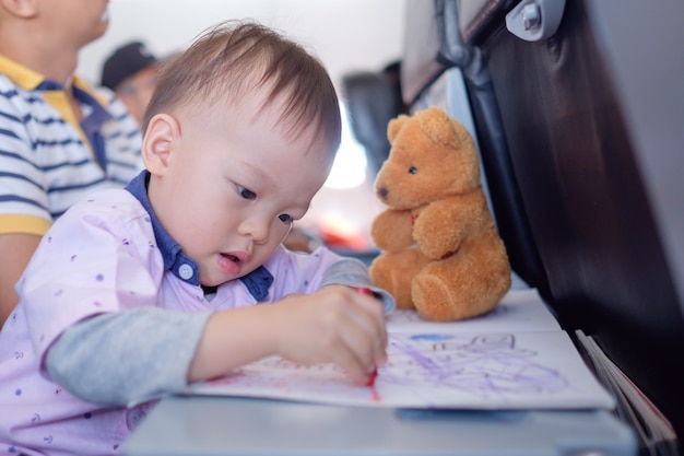 Foto little asiantoddler boy colorear en libro para colorear con lápices de colores durante el vuelo en avión