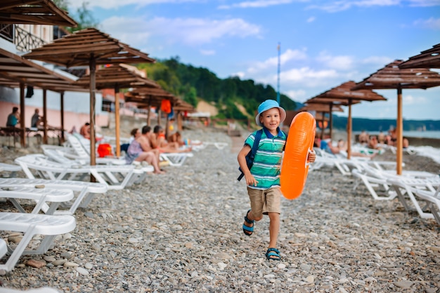 Little Boy de 6 años con un sombrero con un círculo naranja inflable corre