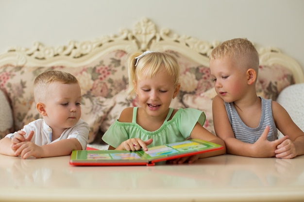 Little Boys and Girl Reading Book en Table at Home