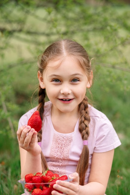 Little Girl Holding plate con fresas en la naturaleza Concepto de agricultura y jardinería Vegano vegetariano Vertical