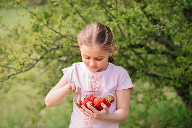 Little Girl Holding plate con fresas en la naturaleza Concepto de agricultura y jardinería Vegano vegetariano