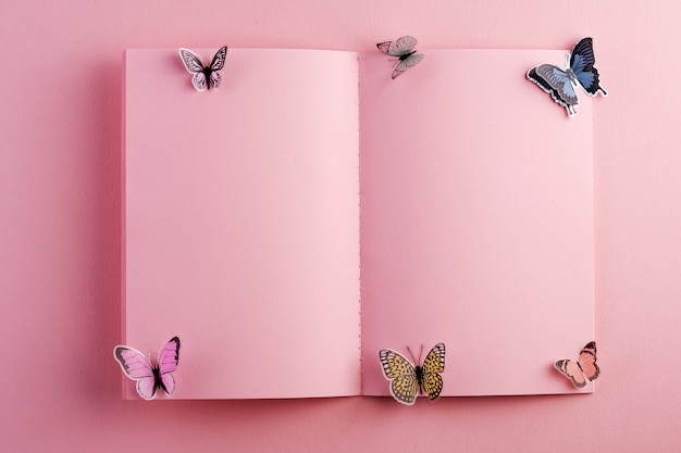 Foto livro aberto em branco na superfície rosa com borboleta artificial