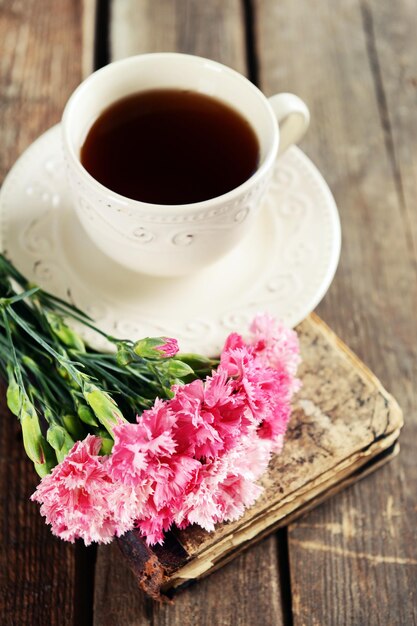 Livro antigo com lindas flores e uma xícara de chá na mesa de madeira close-up