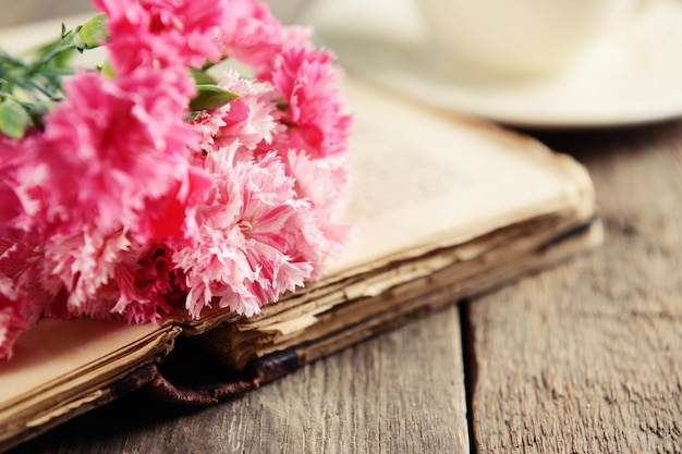 Livro antigo com lindas flores e uma xícara de chá na mesa de madeira close-up